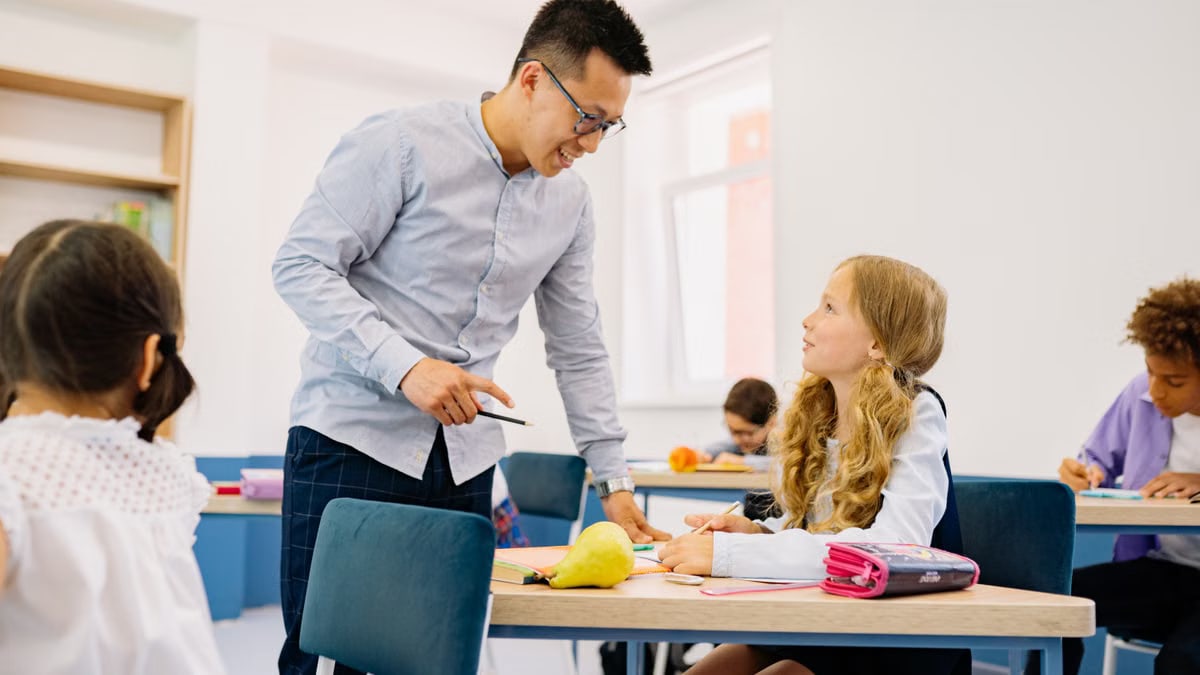 A male teacher interacting with diverse students in a bright classroom setting, promoting active learning.